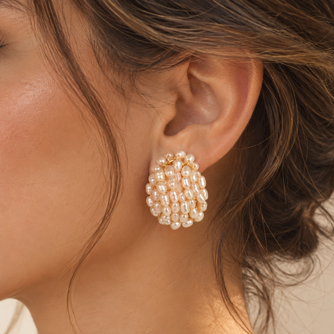 A close-up of a model's ear wearing a cluster of gold and pearl stud earrings.